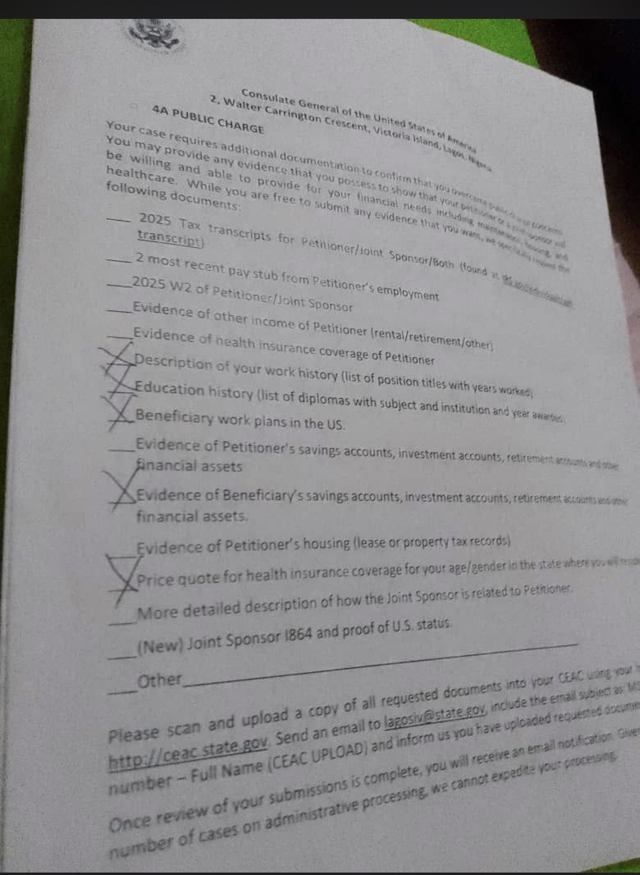 Photograph of a 221(g) public charge checklist headed "4A PUBLIC CHARGE" from the Consulate General of the United States, Walter Carrington Crescent, Victoria Island, Lagos. Below a preamble about overcoming public charge concerns, a list of requestable documents runs down the page with a blank line beside each. Five are ticked: description of work history, education history, beneficiary work plans in the US, evidence of the beneficiary's savings, investment and retirement accounts, and a price quote for health insurance coverage for the applicant's age and gender in the state where they will reside. Unticked entries include tax transcripts, pay stubs, W-2, other petitioner income, petitioner health insurance, petitioner assets, petitioner housing, how the joint sponsor is related to the petitioner, and a new joint sponsor I-864. Instructions at the foot direct the applicant to upload to ceac.state.gov and email lagosiv@state.gov.